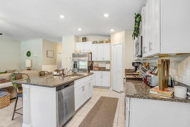 kitchen with tasteful backsplash, stainless steel appliances, a kitchen island with sink, white cabinetry, and a breakfast bar area