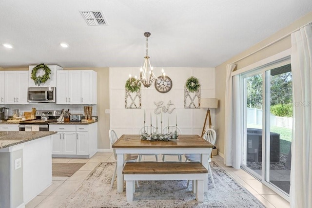 kitchen featuring appliances with stainless steel finishes, dark stone counters, light tile patterned floors, white cabinets, and a chandelier