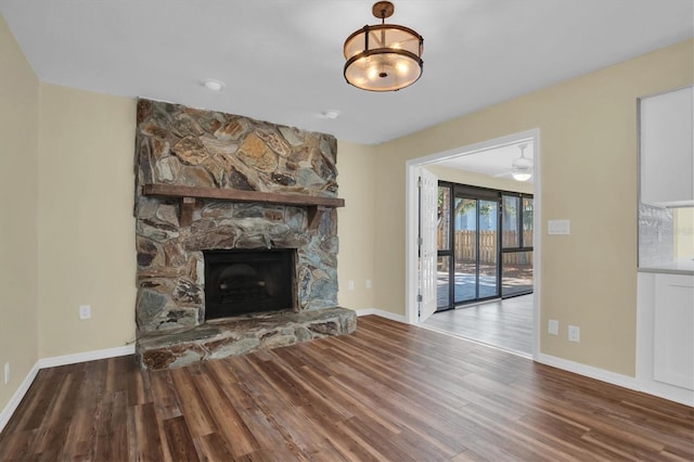 unfurnished living room featuring hardwood / wood-style flooring, ceiling fan, and a stone fireplace