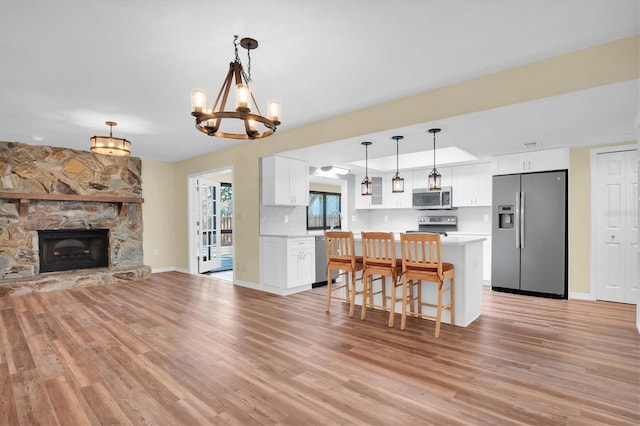 kitchen with appliances with stainless steel finishes, an inviting chandelier, white cabinets, a stone fireplace, and hanging light fixtures