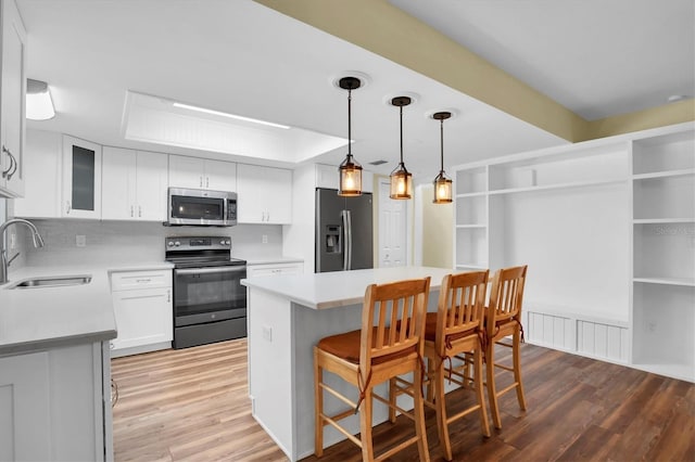 kitchen with sink, a breakfast bar area, light hardwood / wood-style flooring, white cabinetry, and stainless steel appliances