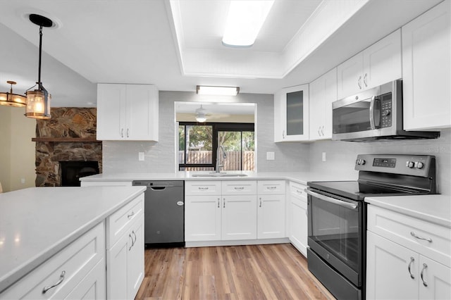 kitchen with stainless steel appliances, white cabinetry, a stone fireplace, and sink