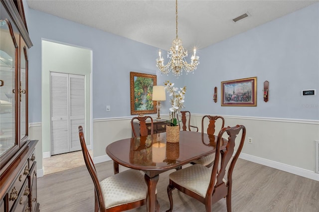 dining space featuring light hardwood / wood-style floors, a textured ceiling, and a notable chandelier