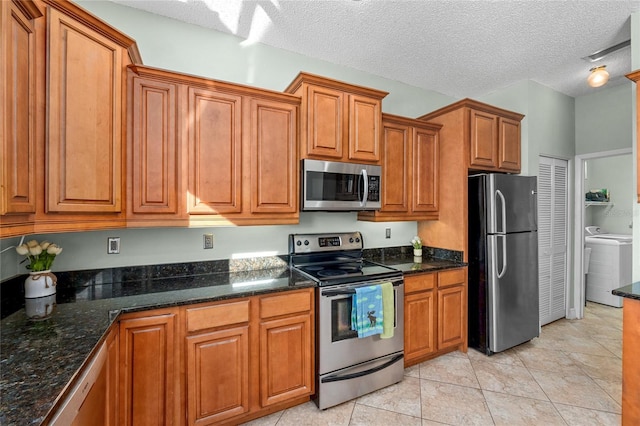 kitchen featuring dark stone counters, a textured ceiling, stainless steel appliances, light tile patterned floors, and washing machine and dryer