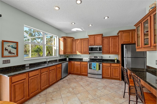 kitchen with sink, a textured ceiling, appliances with stainless steel finishes, and dark stone counters