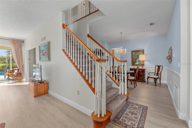 stairs with an inviting chandelier, a textured ceiling, and hardwood / wood-style flooring