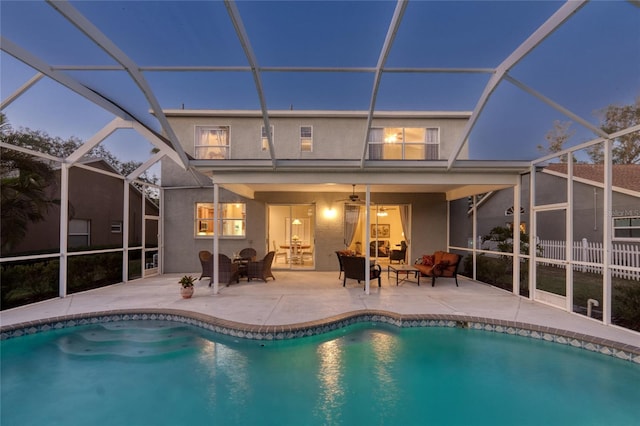 back house at dusk featuring glass enclosure, ceiling fan, outdoor lounge area, and a patio