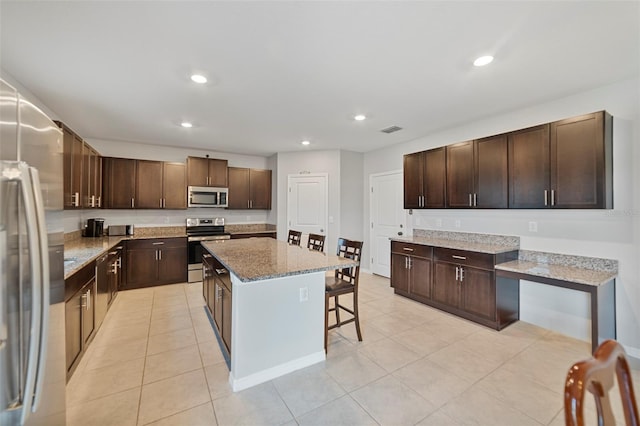 kitchen with a breakfast bar area, a center island, stainless steel appliances, and dark brown cabinets