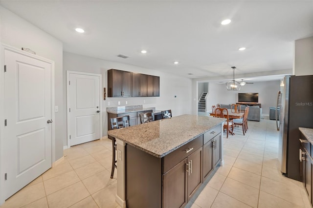 kitchen featuring stainless steel refrigerator with ice dispenser, light stone counters, a breakfast bar, ceiling fan, and a kitchen island