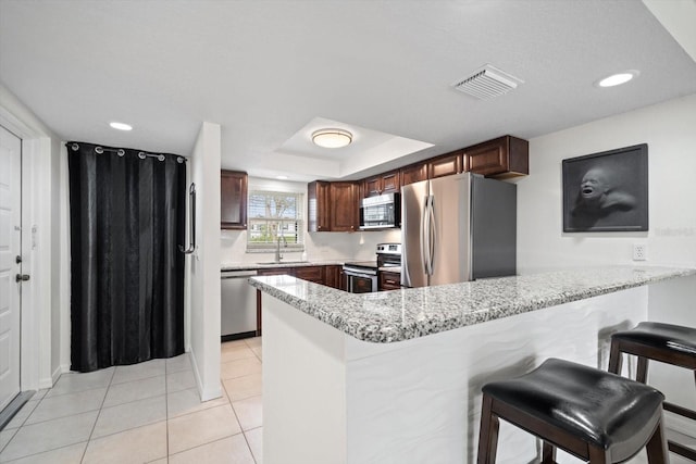 kitchen with sink, stainless steel appliances, a kitchen breakfast bar, kitchen peninsula, and a tray ceiling