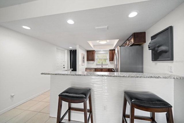 kitchen featuring kitchen peninsula, stainless steel fridge, and light stone counters