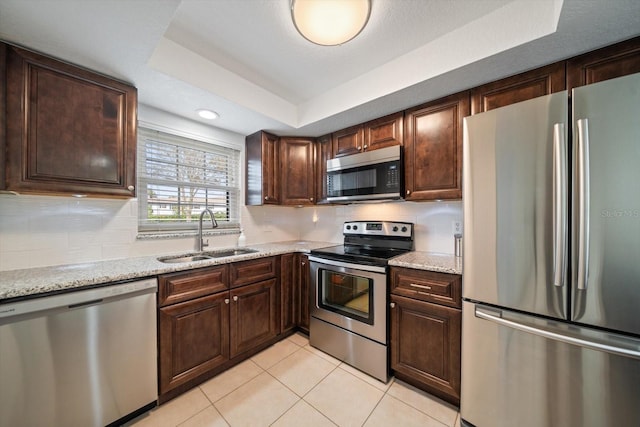 kitchen with light stone countertops, stainless steel appliances, a raised ceiling, sink, and light tile patterned flooring