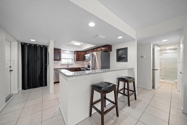 kitchen with kitchen peninsula, light stone counters, light tile patterned flooring, and stainless steel appliances