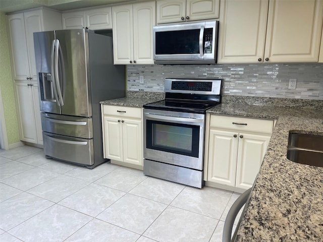 kitchen featuring appliances with stainless steel finishes, tasteful backsplash, light tile patterned floors, and dark stone countertops