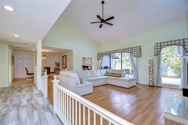 living room with ceiling fan with notable chandelier, a textured ceiling, high vaulted ceiling, and light hardwood / wood-style flooring