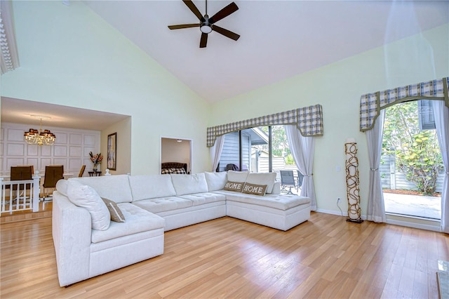 living room with light wood-type flooring, ceiling fan with notable chandelier, and high vaulted ceiling