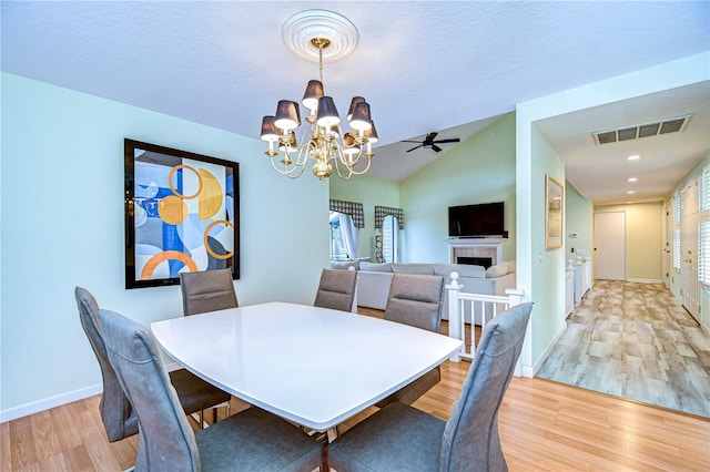 dining room featuring ceiling fan with notable chandelier, light hardwood / wood-style flooring, and lofted ceiling