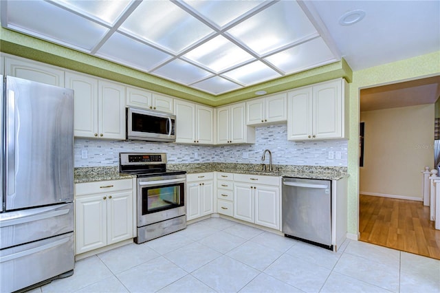 kitchen with white cabinets, sink, light stone countertops, light tile patterned flooring, and stainless steel appliances