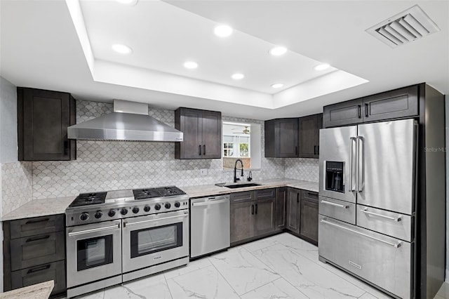 kitchen featuring sink, a tray ceiling, high end appliances, and wall chimney range hood