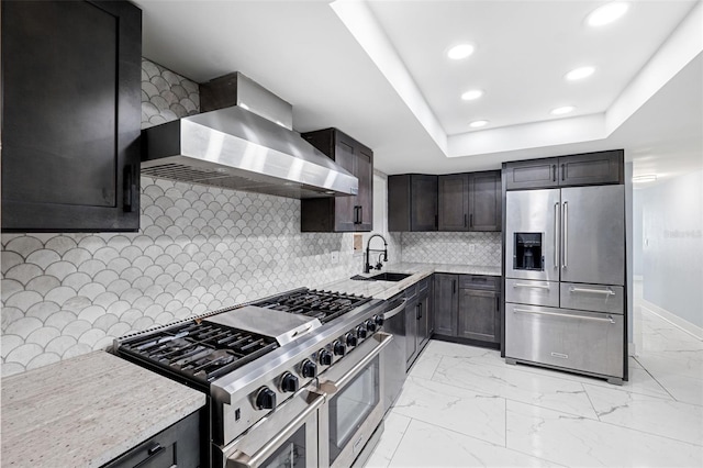 kitchen featuring backsplash, a raised ceiling, sink, wall chimney exhaust hood, and appliances with stainless steel finishes