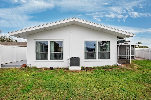 rear view of property featuring a lawn, a sunroom, and central AC unit