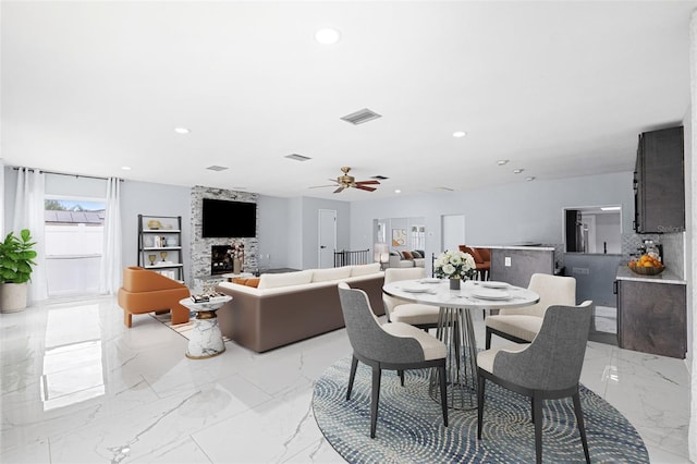 dining room featuring ceiling fan and a stone fireplace