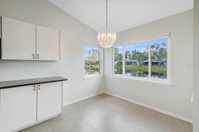 unfurnished dining area featuring a water view, an inviting chandelier, lofted ceiling, and light tile patterned flooring