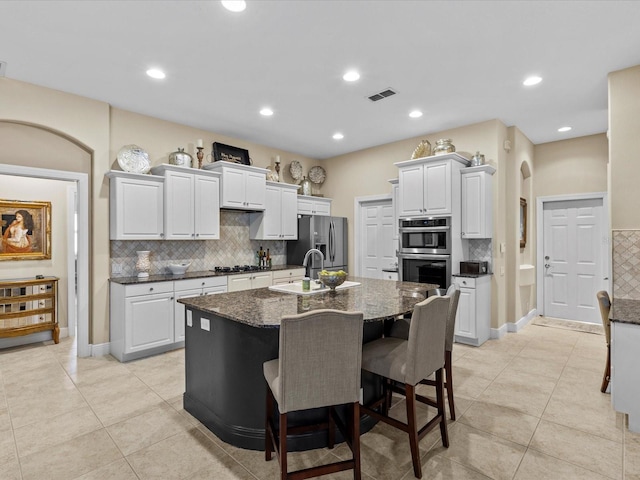 kitchen with white cabinetry, dark stone counters, a breakfast bar area, a kitchen island with sink, and appliances with stainless steel finishes