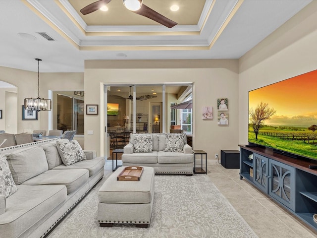 tiled living room with crown molding, ceiling fan with notable chandelier, and a raised ceiling