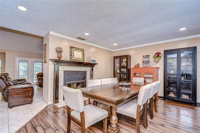 dining area featuring a tile fireplace, light tile patterned floors, a textured ceiling, and ornamental molding