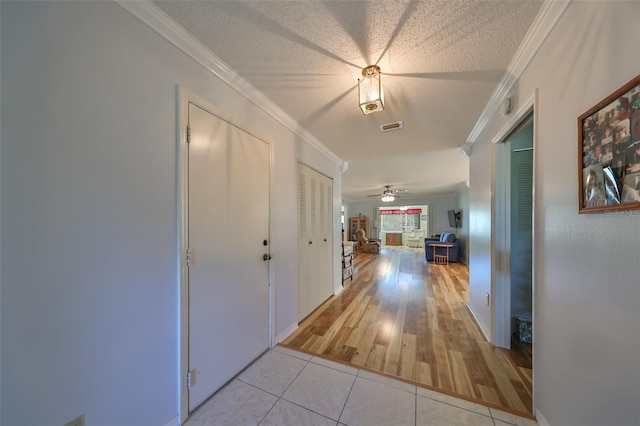 corridor with crown molding, light tile patterned floors, and a textured ceiling