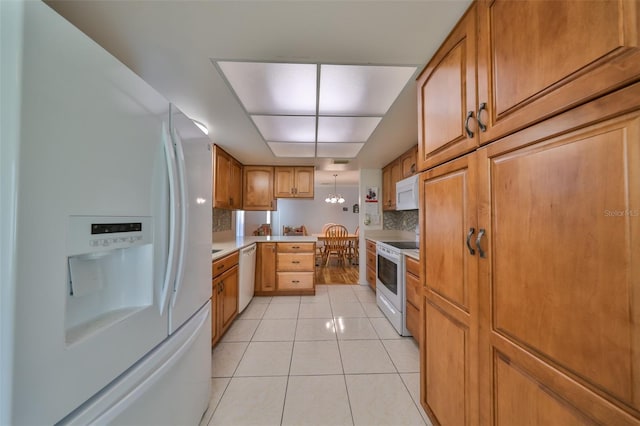 kitchen with tasteful backsplash, white appliances, light tile patterned floors, a chandelier, and hanging light fixtures