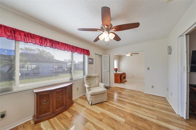 living area featuring a textured ceiling, light hardwood / wood-style floors, and ceiling fan