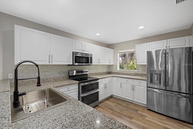 kitchen featuring light stone counters, stainless steel appliances, sink, light hardwood / wood-style floors, and white cabinetry