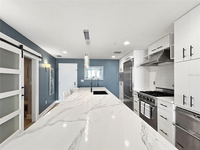 kitchen featuring extractor fan, sink, pendant lighting, a barn door, and built in appliances