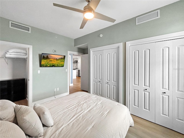 bedroom with light hardwood / wood-style floors, ceiling fan, and multiple closets