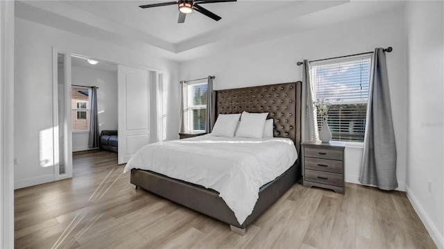 bedroom with light hardwood / wood-style floors, ceiling fan, and a tray ceiling