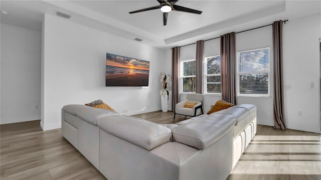 living room featuring a raised ceiling, ceiling fan, and light hardwood / wood-style floors