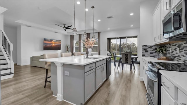 kitchen with stainless steel appliances, a kitchen island with sink, sink, white cabinetry, and hanging light fixtures