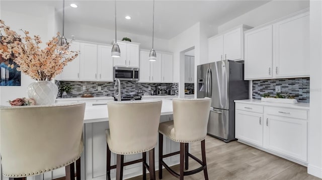 kitchen with white cabinetry, hanging light fixtures, a kitchen bar, a kitchen island with sink, and appliances with stainless steel finishes