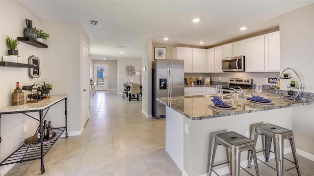 kitchen with stainless steel appliances, kitchen peninsula, dark stone counters, a kitchen bar, and white cabinets