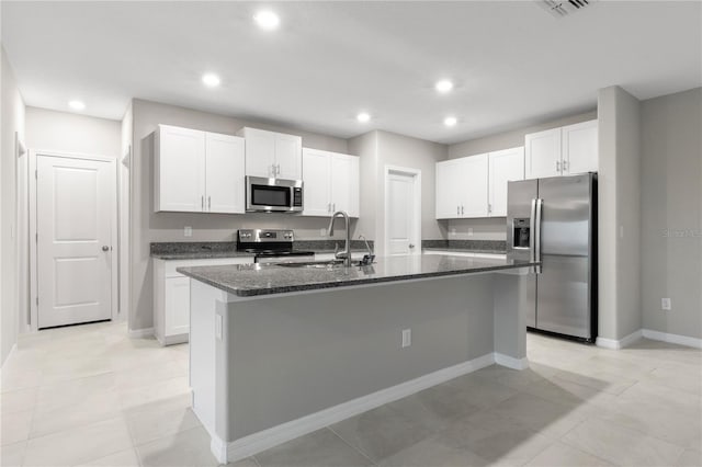 kitchen with dark stone counters, sink, an island with sink, white cabinetry, and stainless steel appliances