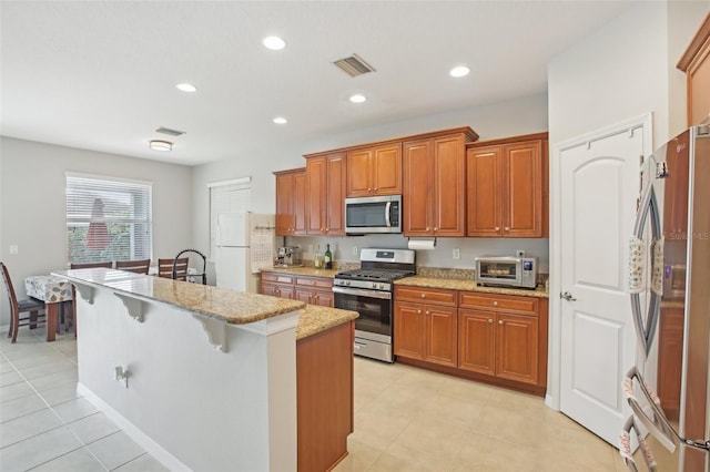 kitchen featuring light stone countertops, appliances with stainless steel finishes, a kitchen breakfast bar, an island with sink, and light tile patterned flooring