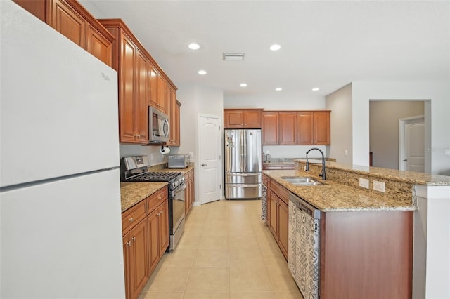 kitchen featuring light stone counters, stainless steel appliances, sink, light tile patterned floors, and an island with sink