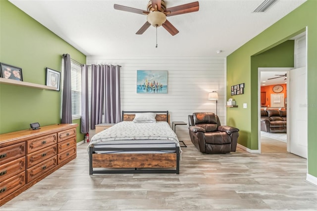 bedroom featuring light hardwood / wood-style floors, ceiling fan, and wooden walls