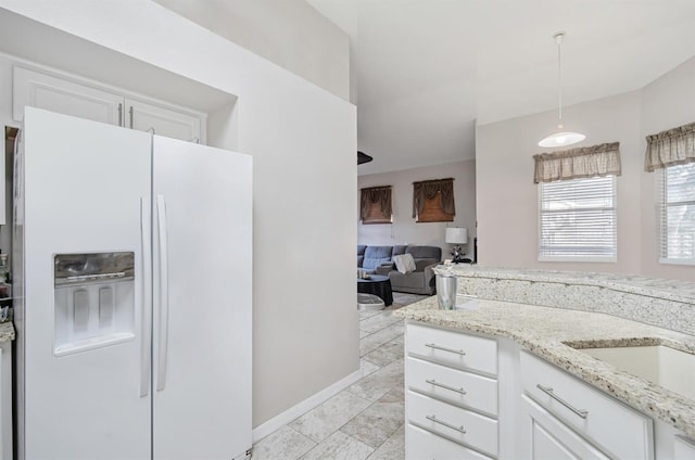 kitchen with sink, hanging light fixtures, white fridge with ice dispenser, light stone counters, and white cabinetry