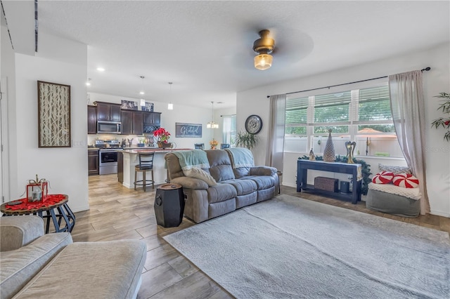 living room featuring ceiling fan with notable chandelier and light hardwood / wood-style flooring