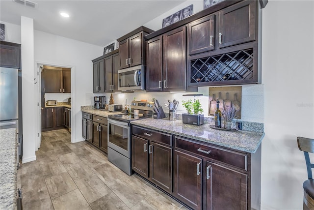 kitchen featuring appliances with stainless steel finishes, backsplash, light stone counters, and dark brown cabinets