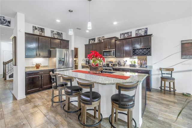 kitchen featuring a kitchen island with sink, a breakfast bar, hanging light fixtures, and appliances with stainless steel finishes