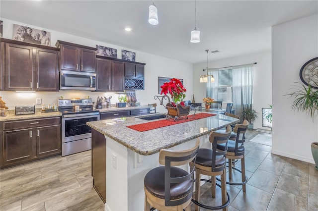 kitchen featuring appliances with stainless steel finishes, a kitchen island with sink, sink, pendant lighting, and a breakfast bar area